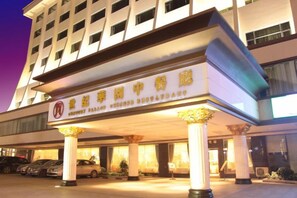 Entrada de hotel con una galería techada, columnas y un letrero con caracteres chinos.