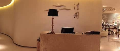 A reception desk with a lamp, a black object on the desk, and a wall with a design.