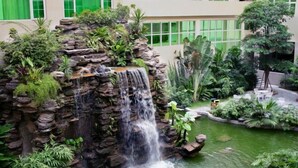 A waterfall feature surrounded by lush greenery and rocks, with a building in the background. - Century Palace Hotel (Huizhou)