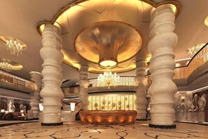 Un'imponente hall con ampie colonne, una zona salotto centrale e lampadari.