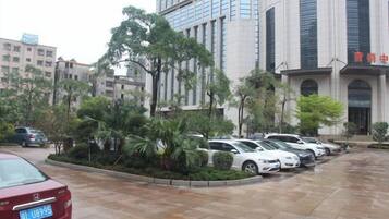 Um estacionamento com vários carros, um edifício com fachada moderna e uma área ajardinada com árvores.