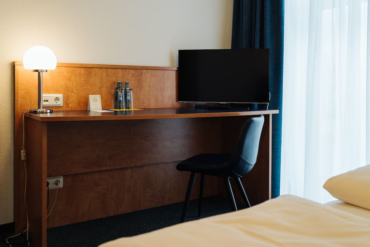 Habitación de hotel con un escritorio de madera, una silla negra, un televisor de pantalla plana y una cama con almohada blanca.