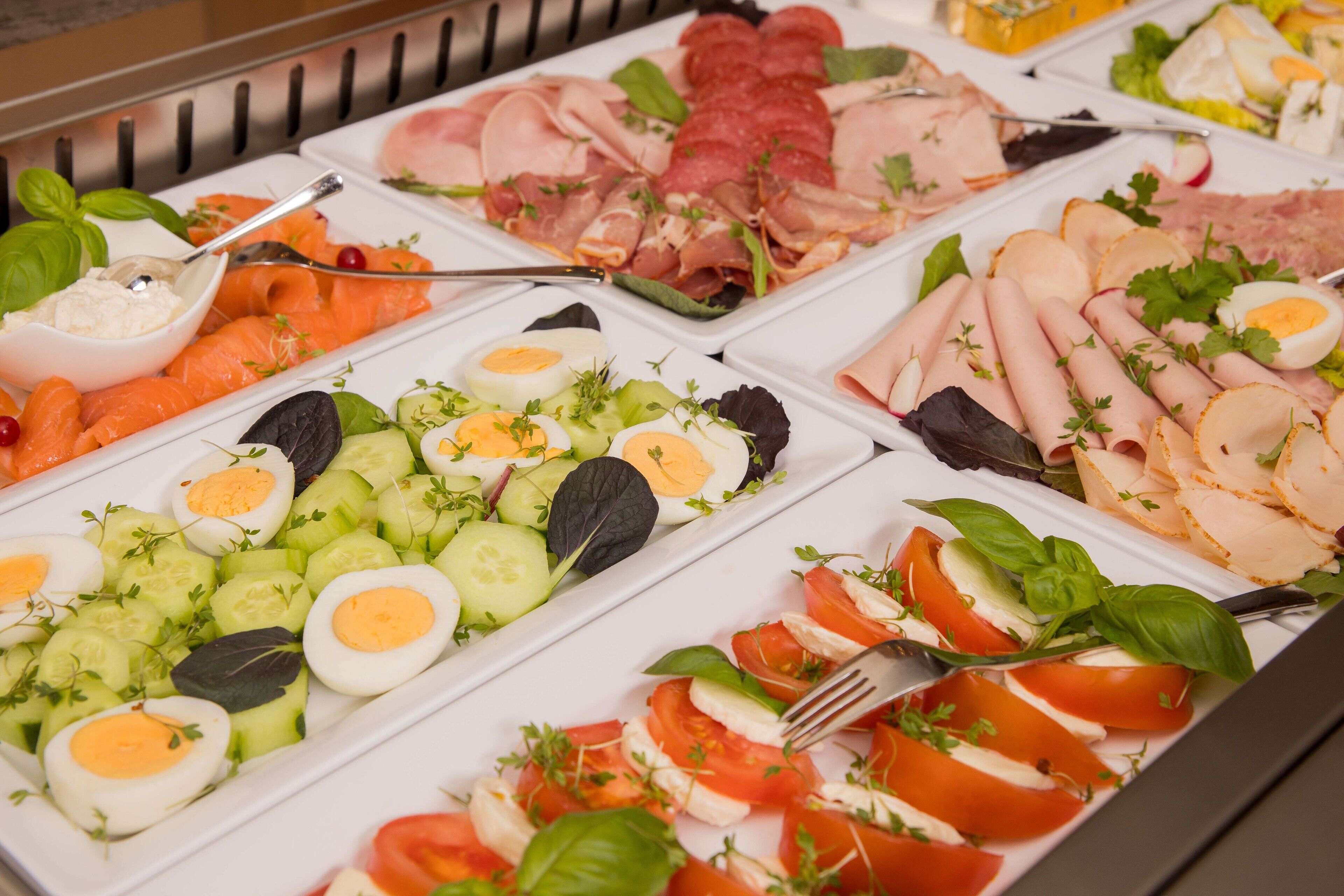 Un bufé con diversas opciones de comida, incluyendo carnes cortadas, quesos y verduras.