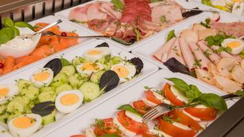 Un bufé con diversas opciones de comida, incluyendo carnes cortadas, quesos y verduras.