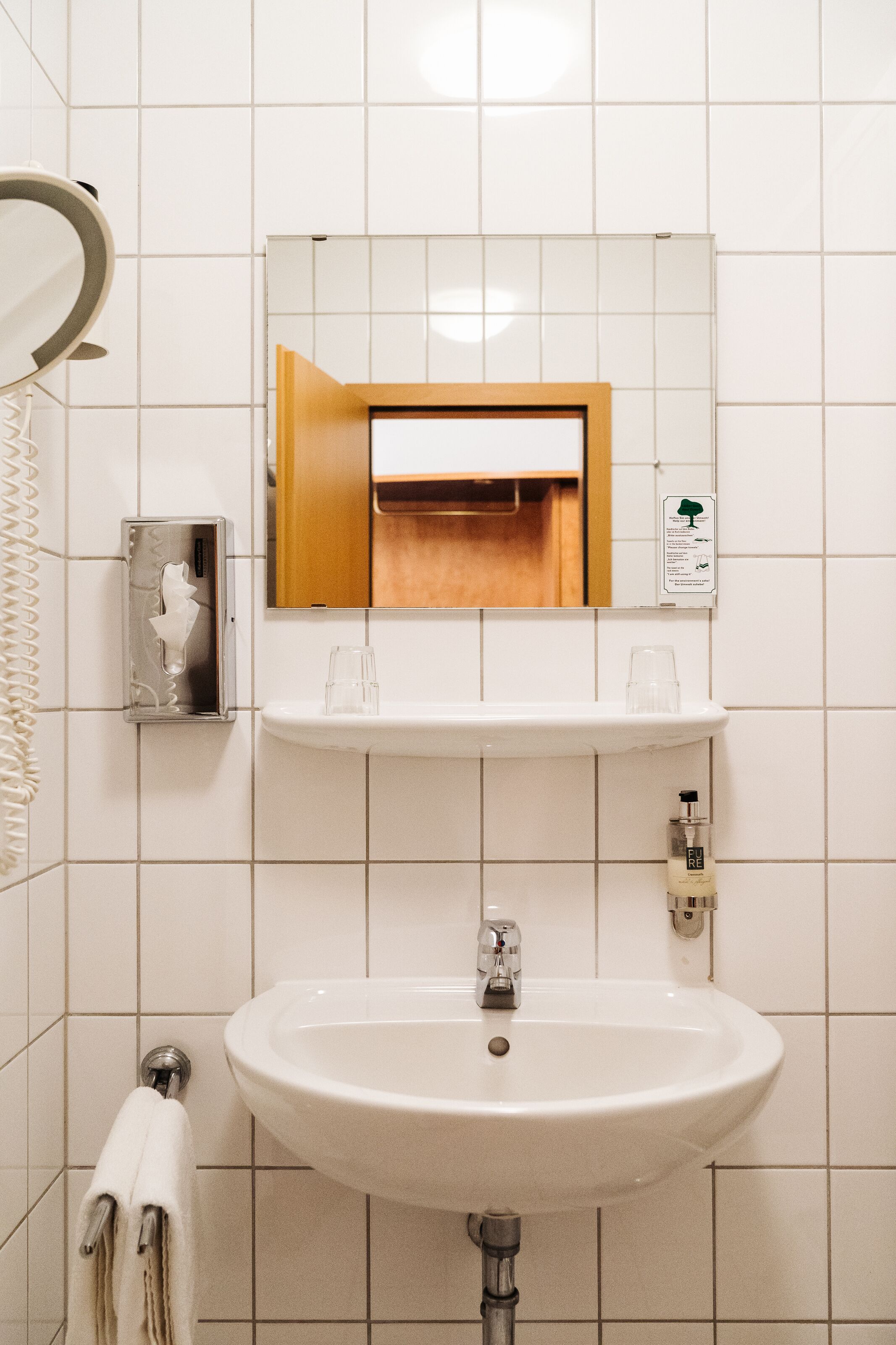 A bathroom with a white sink, a mirror, a towel rack, and a soap dispenser.
