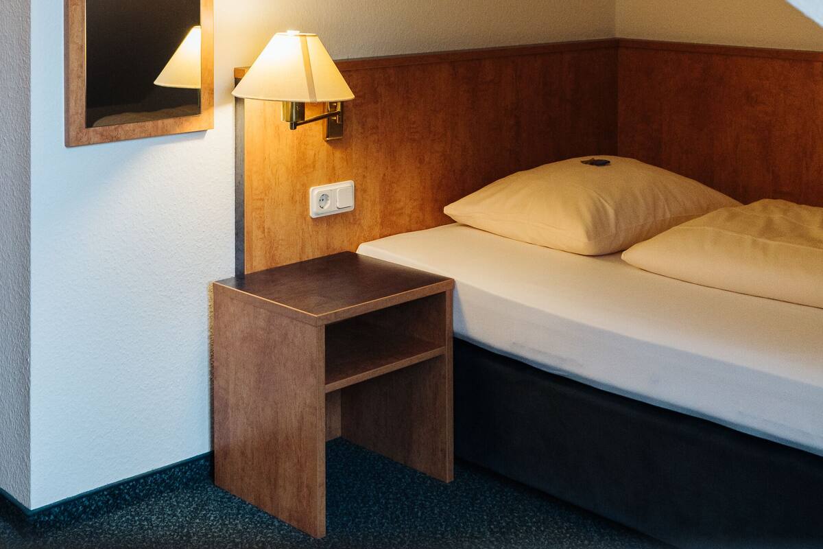 Una habitación de hotel con cama, mesita de noche, lámpara y espejo.