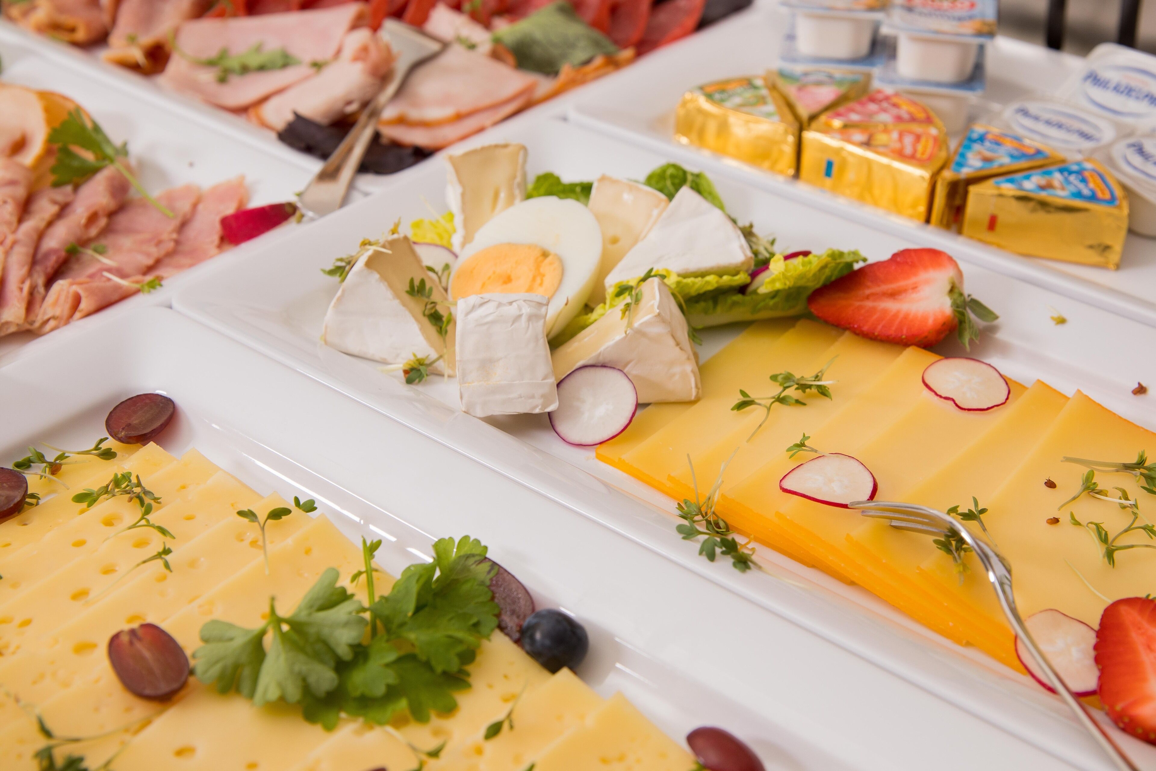 A buffet with various cheeses, meats, and garnishes.