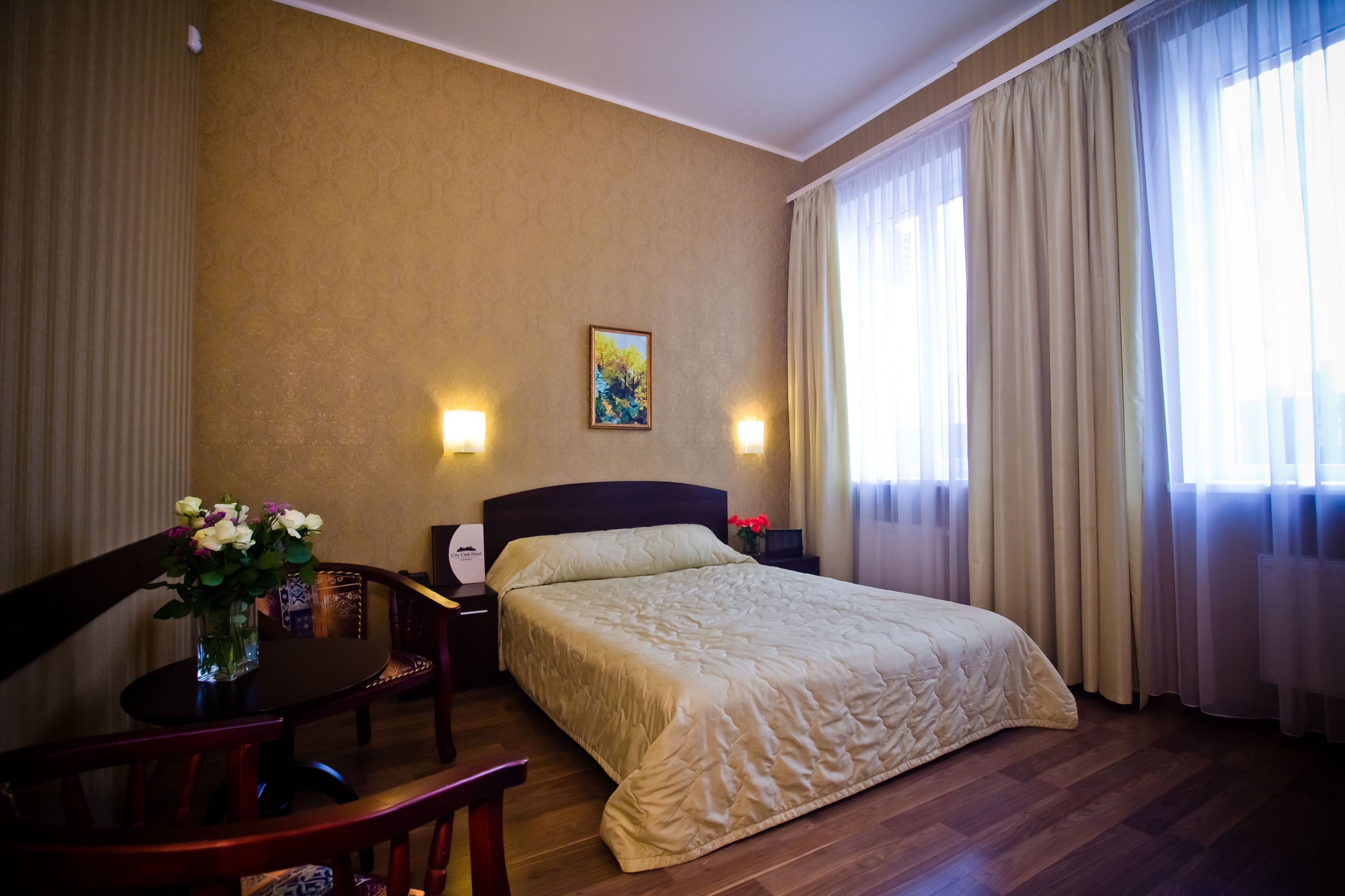 Une chambre d’hôtel avec un lit, un bureau et une chaise, un vase avec des fleurs et un tableau au mur.