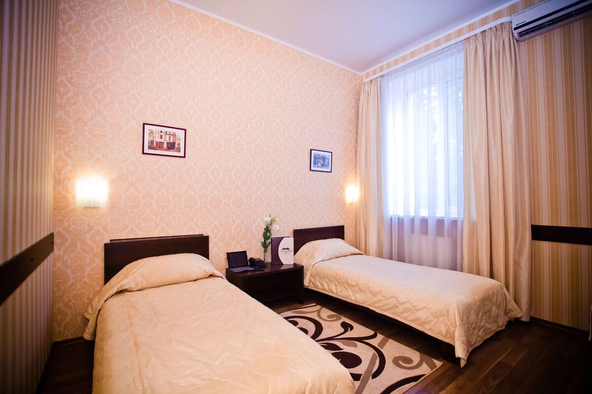 A hotel room with two beds, a nightstand, a framed picture, and a window with curtains.