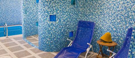 A tiled pool area with blue mosaic walls, a patterned floor, and two blue lounge chairs.