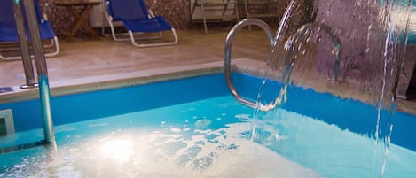 Una piscina interior con agua cristalina, un trampolín y sillas de descanso.