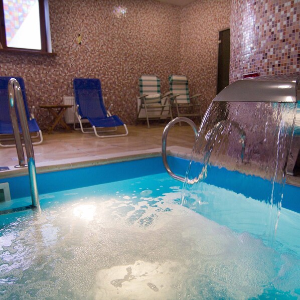 An indoor swimming pool with clear water, a diving board, and lounge chairs.