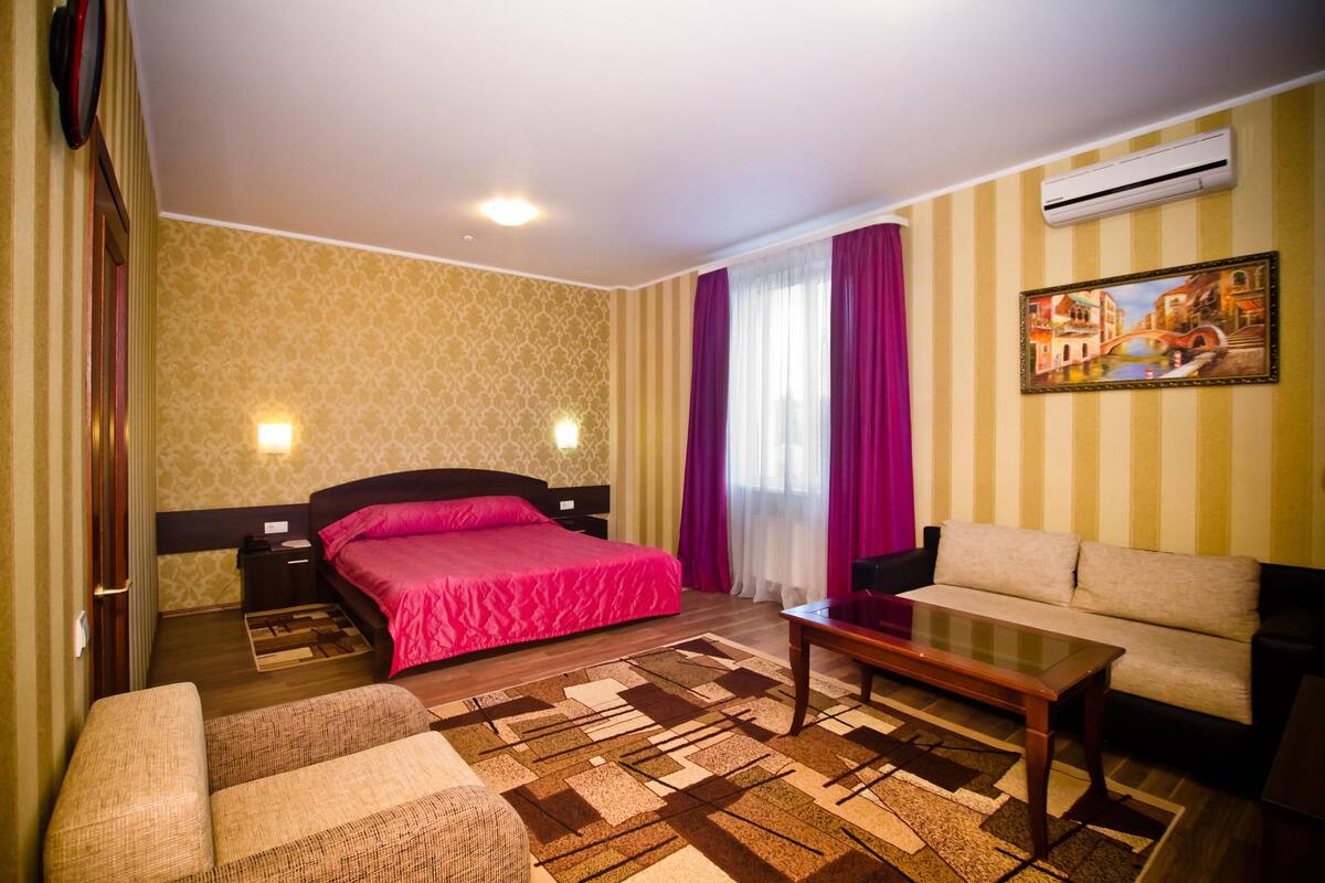 A hotel room with a bed, a sofa, a coffee table, and a painting on the wall.