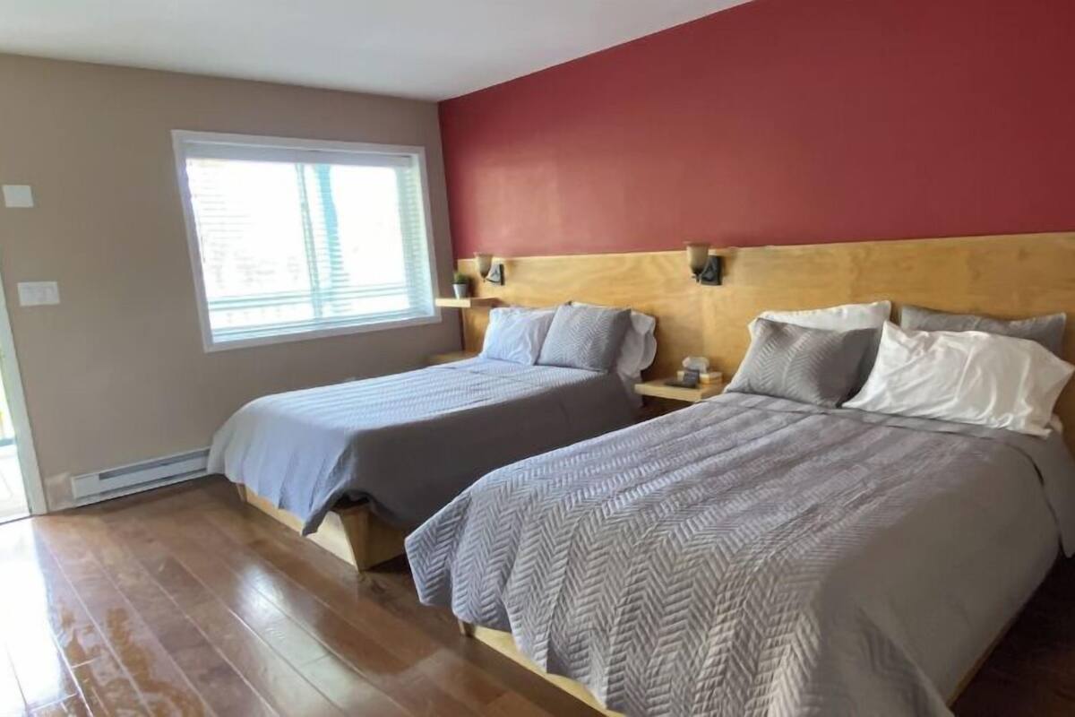 A bedroom with two beds, wooden headboard, a window, and a red accent wall.