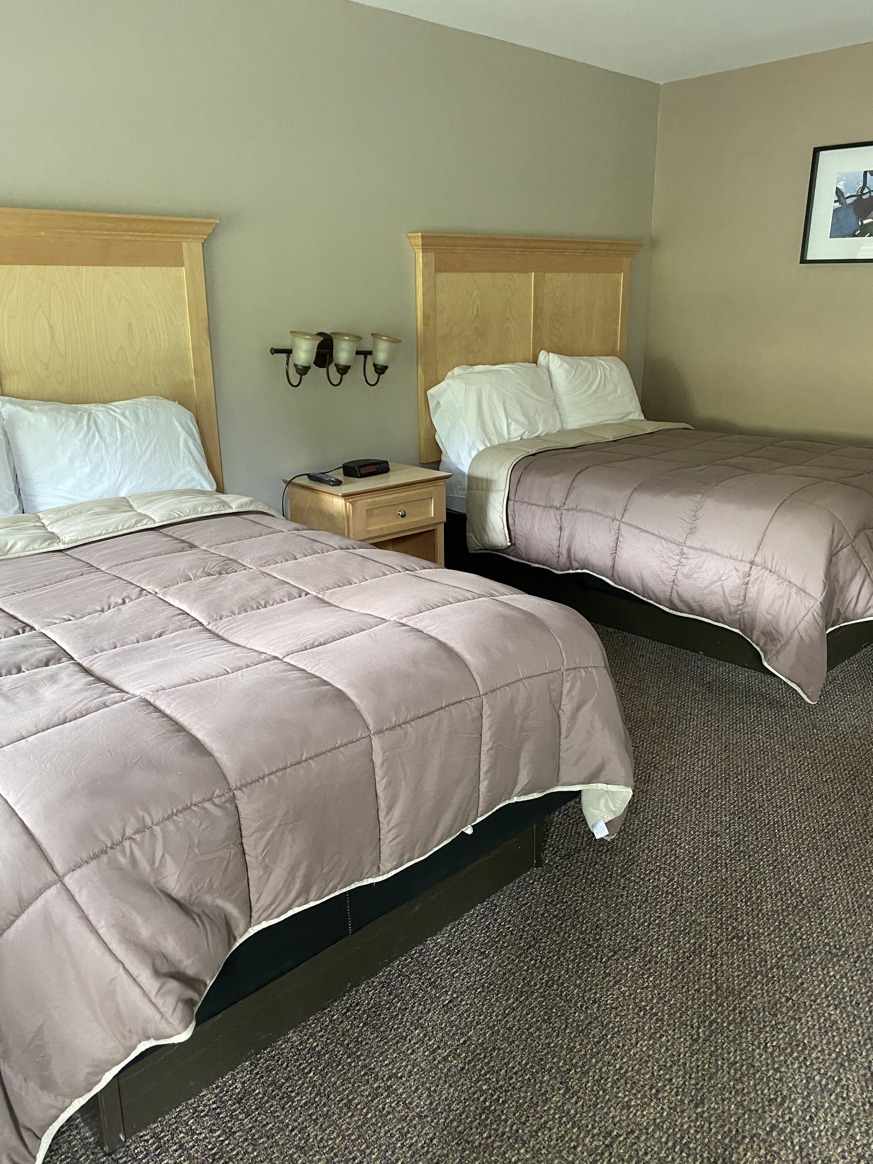 A hotel room with two beds, a nightstand, and a wall-mounted lamp.