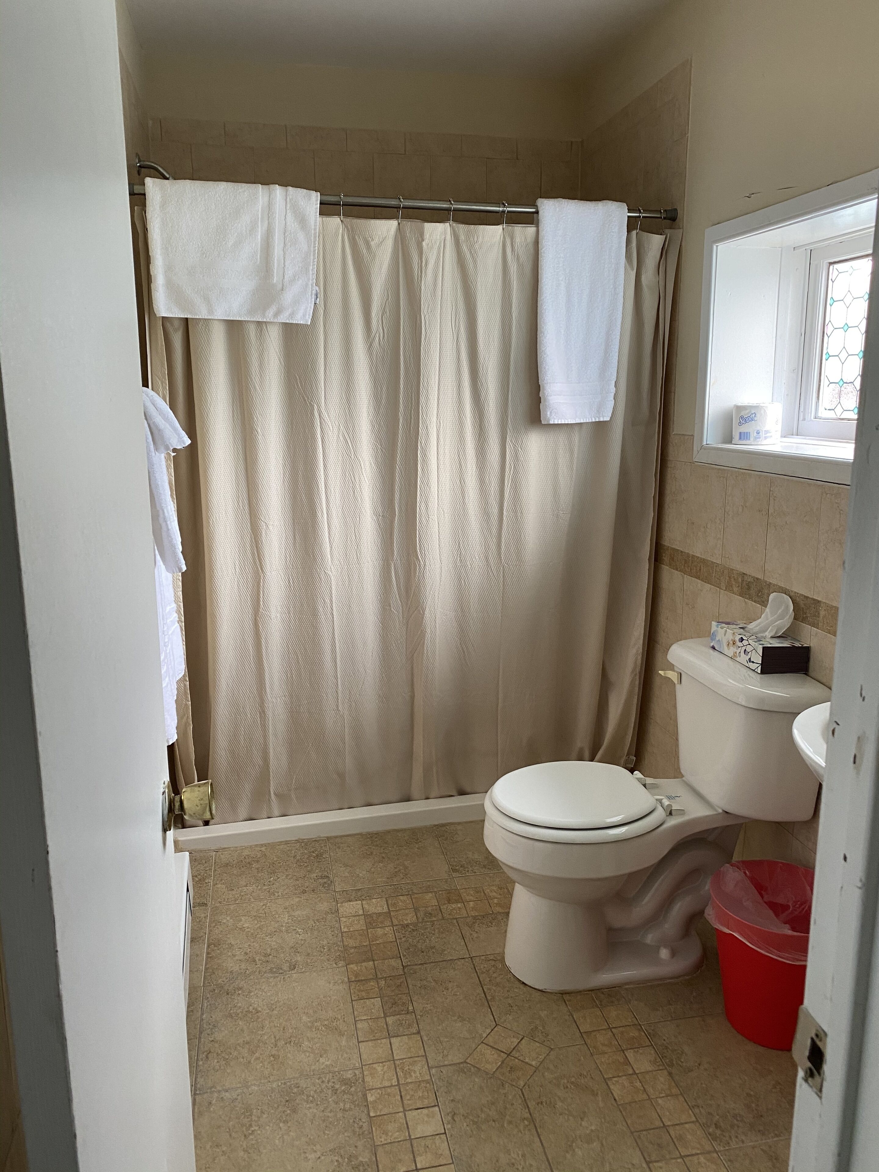 A bathroom with a shower curtain, a toilet, a sink, and a window.