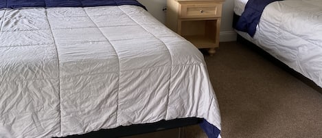 Ein Hotelzimmer mit zwei Betten, Holz-Kopfteilen, einem Nachttisch mit Lampe und einem kleinen Holztisch.