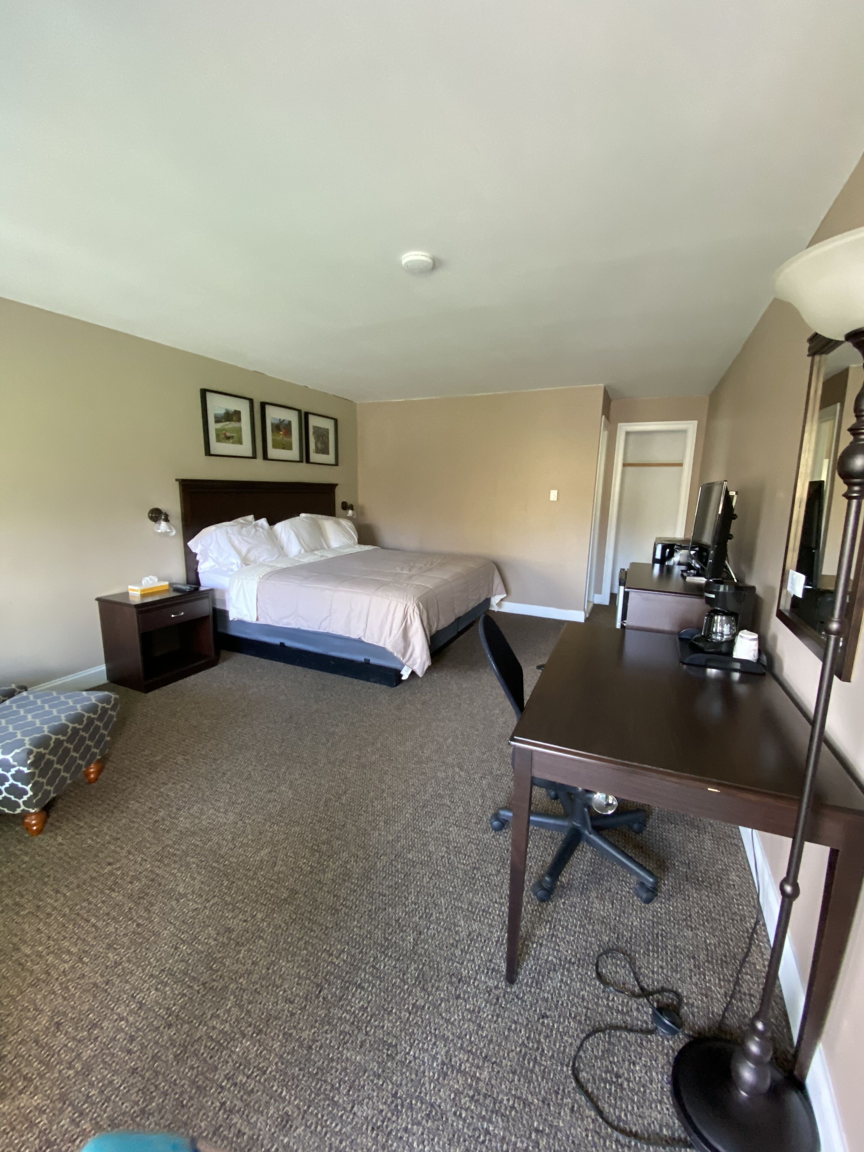 Una habitación de hotel con cama, escritorio, silla, mesita de noche y lámpara.