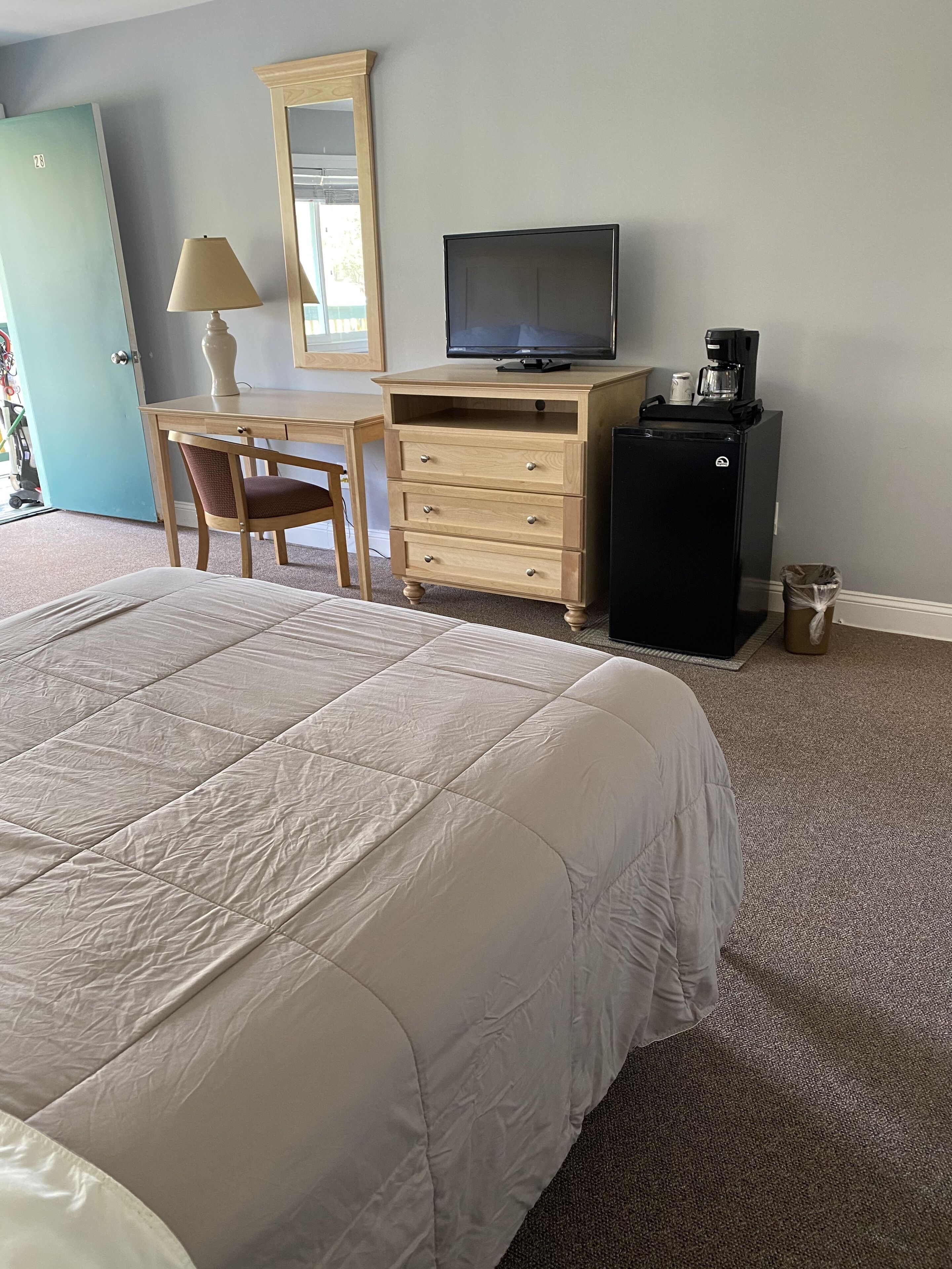 Une chambre d’hôtel avec un grand lit, un bureau avec une chaise, une télévision, une machine à café et un réfrigérateur.