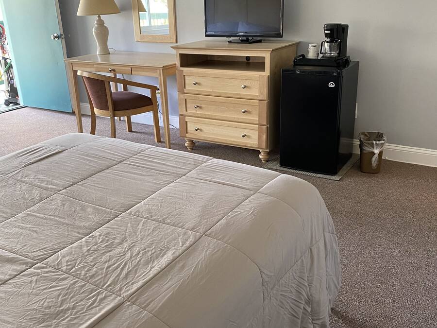 Habitación de hotel con una cama grande, un escritorio con una silla, televisor, cafetera y refrigerador.