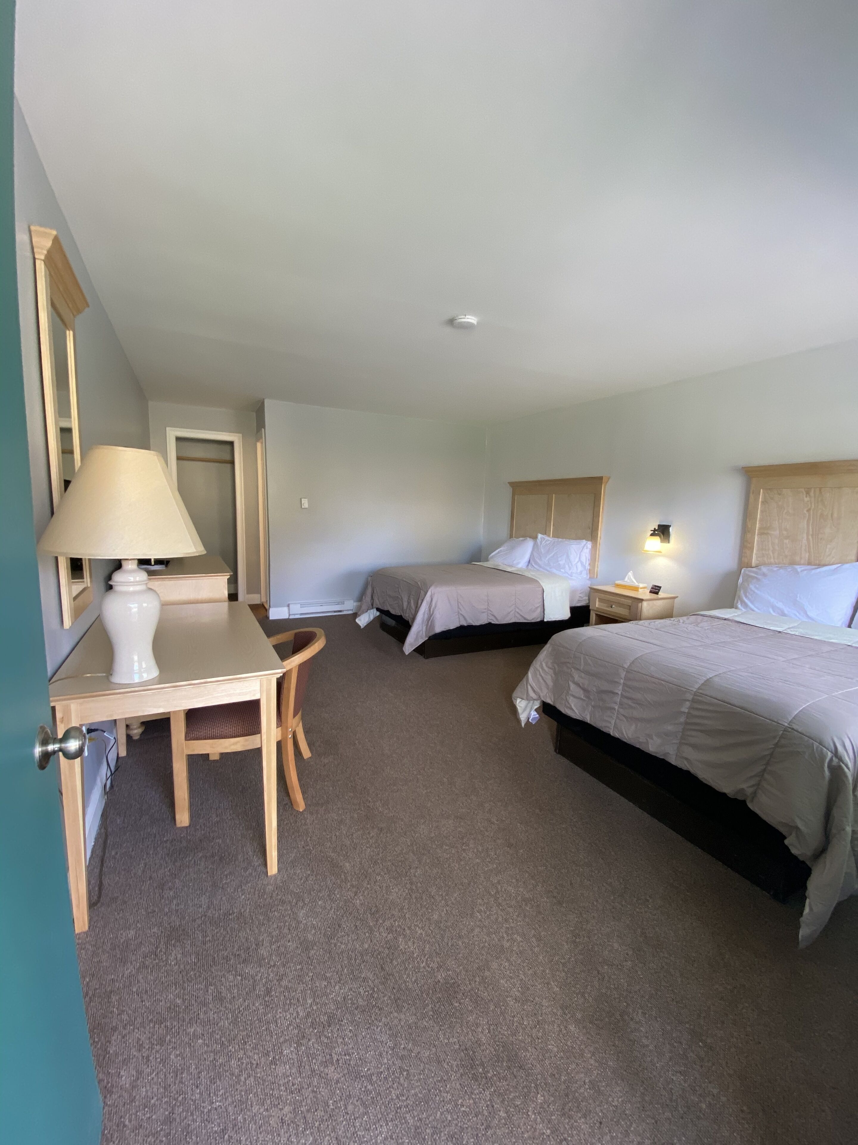 A hotel room with two beds, a desk with a lamp, a chair, and a small table.