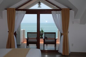 Un dormitorio con un ventanal grande, una cama y dos sillas de madera orientadas al mar.
