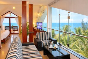 Habitación de hotel con balcón, cama, sofá, televisor y vista al océano.
