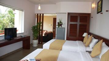 A hotel room with two beds, a TV, a desk, a plant, and a view of palm trees.