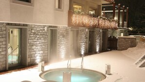 A heated outdoor pool surrounded by snow, with stone walls and a glass door entrance. - Miramonti Park Hotel (Bormio)