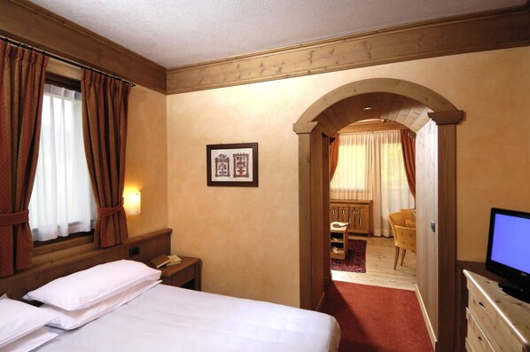 Habitación de hotel con cama, escritorio, silla, televisor y un arco que da a otra habitación.