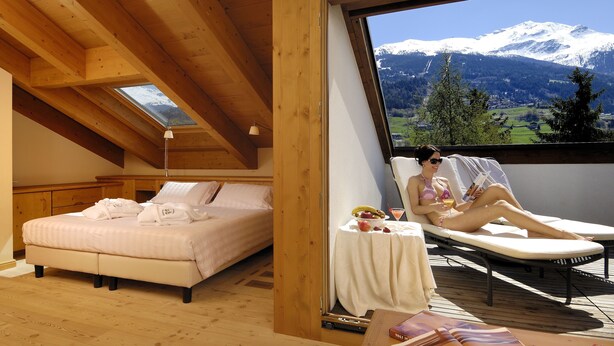 A bedroom with a bed, a small table with a fruit bowl, and a view of a mountain. - Miramonti Park Hotel (Bormio)