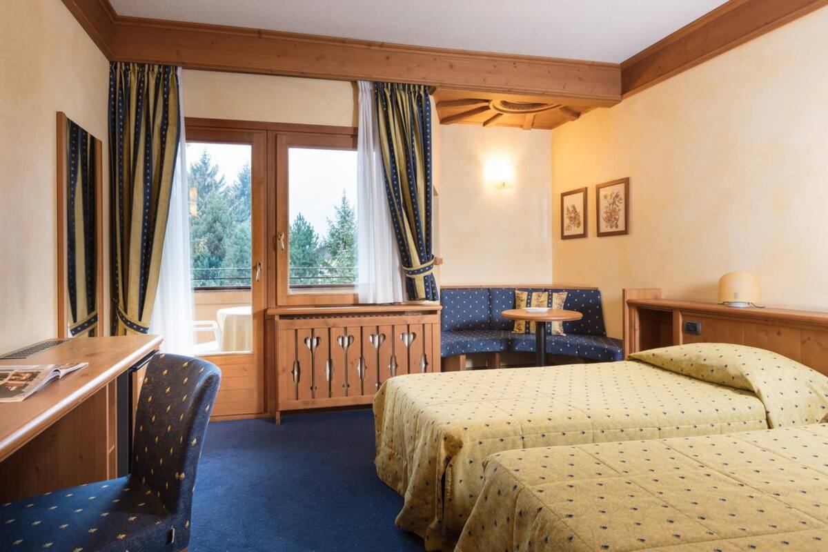 Une pièce comprenant un lit, un bureau, une chaise, une petite table et une fenêtre avec des rideaux.