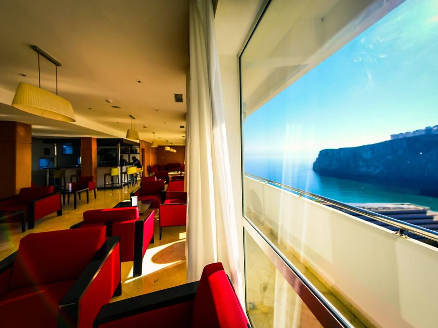 A modern interior with red seating and a large window overlooking a cliff.