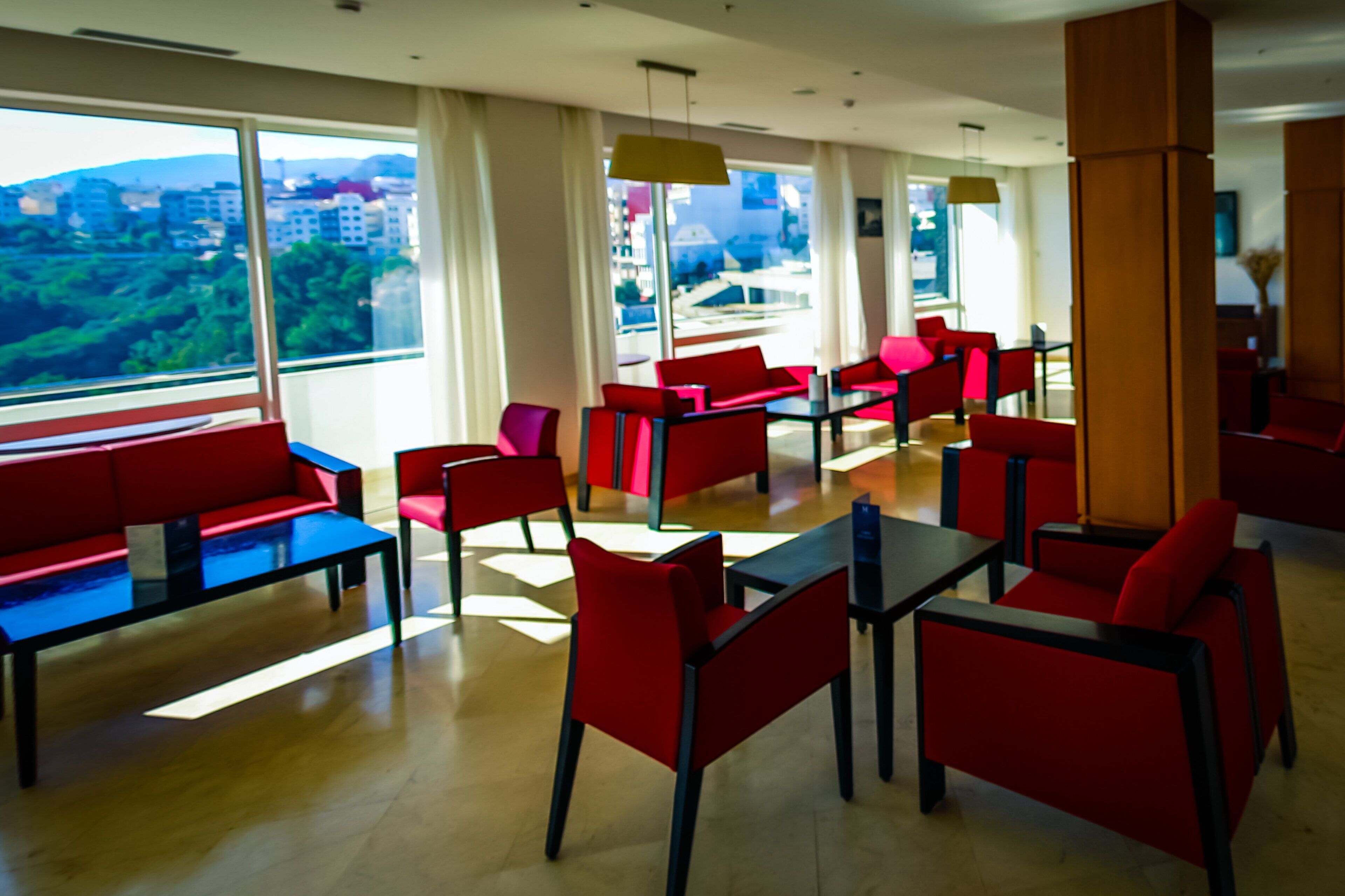 A modern dining area with red and blue furniture, large windows offering a city view, and a clean, bright interior.