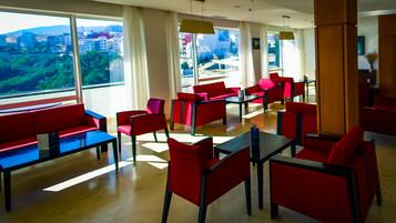 A modern dining area with red and blue furniture, large windows offering a city view, and a clean, bright interior.