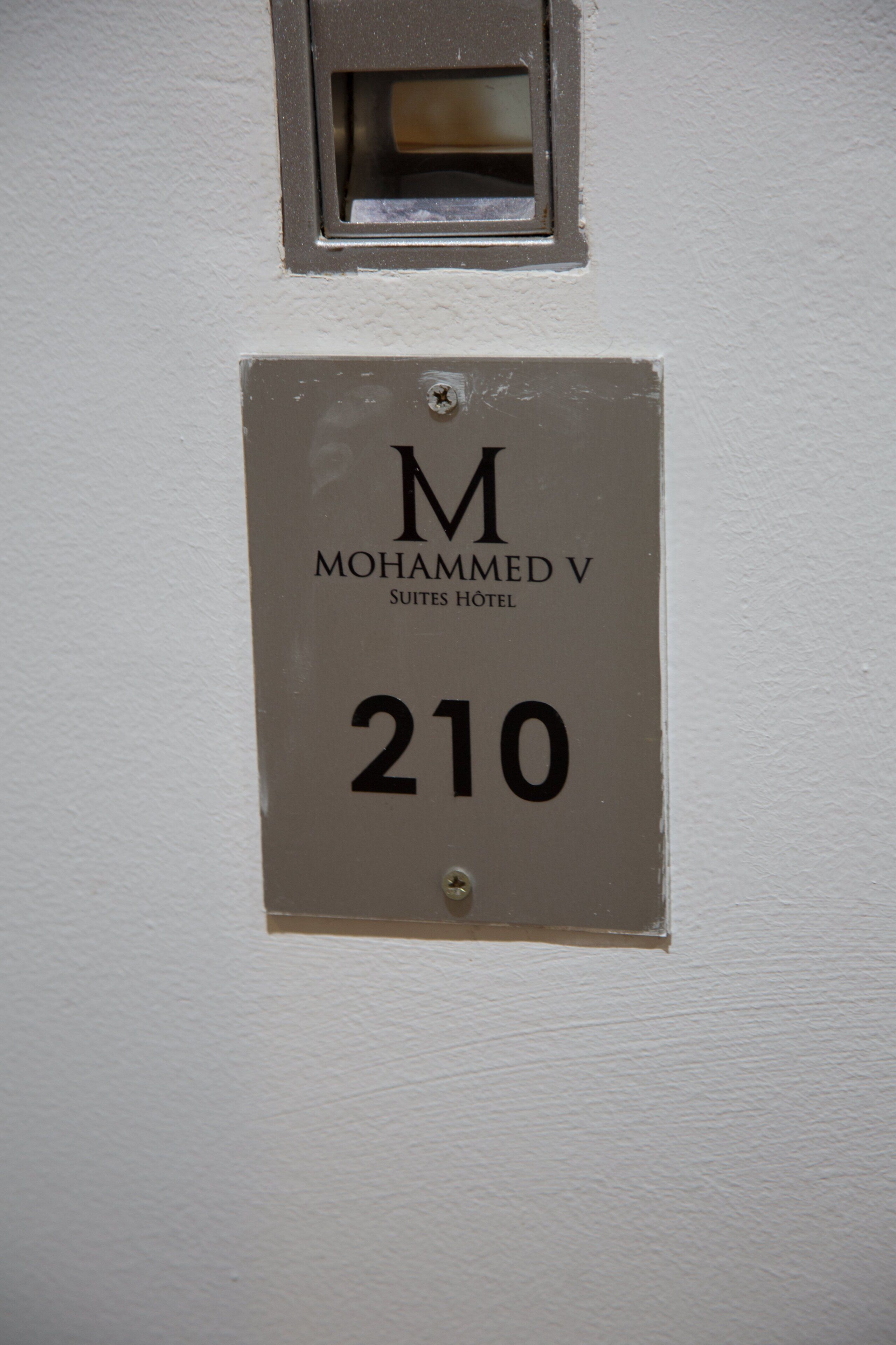 A hotel room number sign for "Mohammed V Suites Hotel" with the number 210.