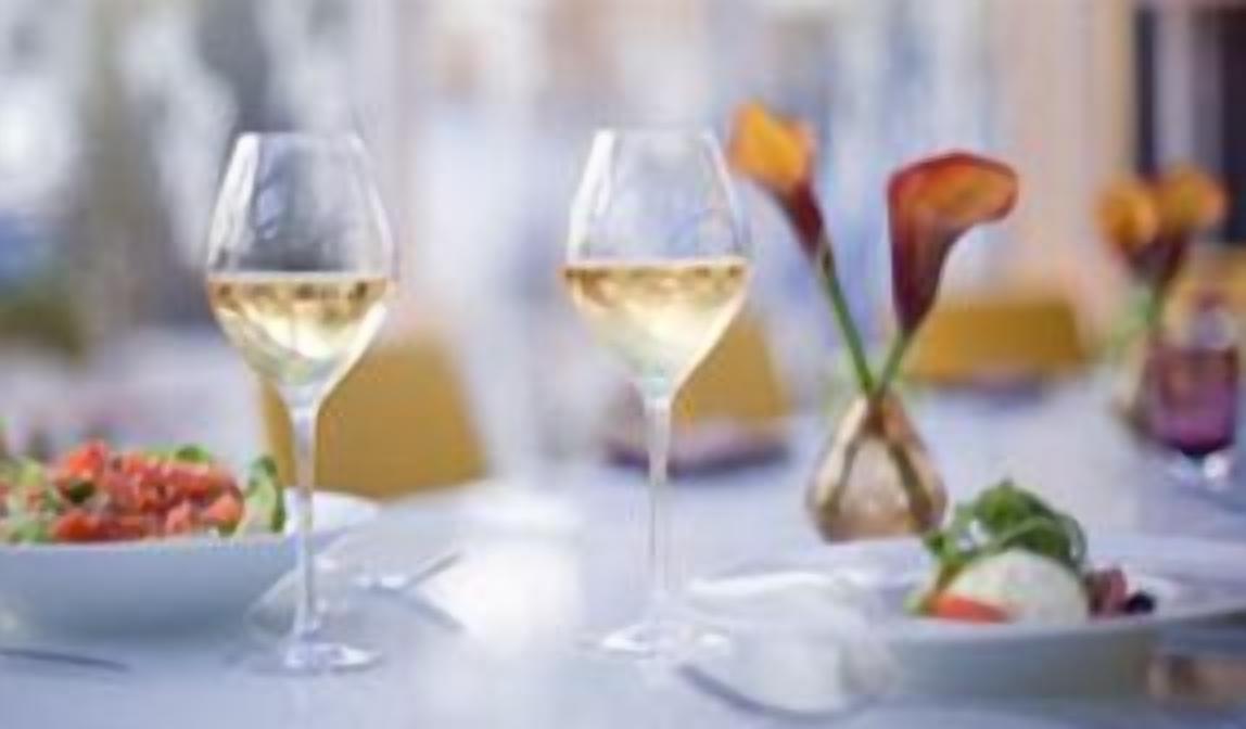 Une table à manger avec deux verres de vin blanc, un saladier et un vase rempli de fleurs.