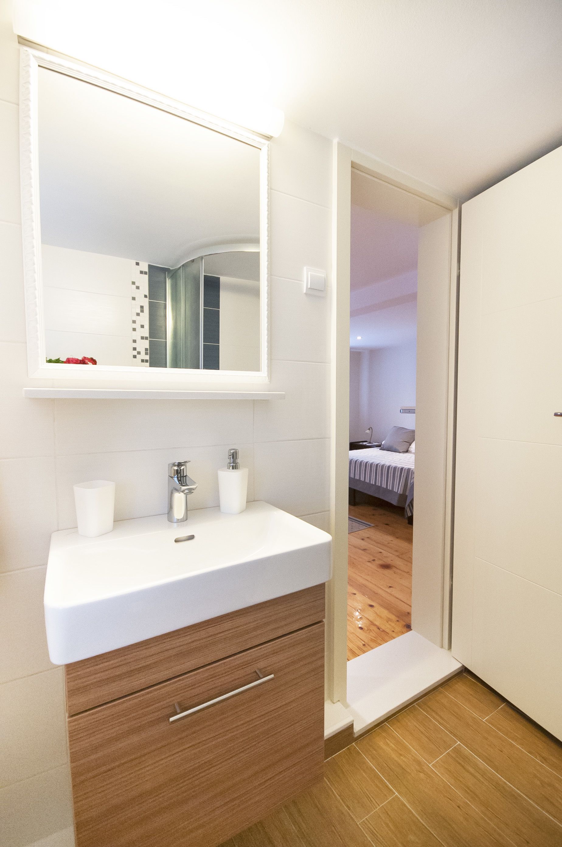 A bathroom with a white sink, two white cups, a mirror, and a wooden cabinet.