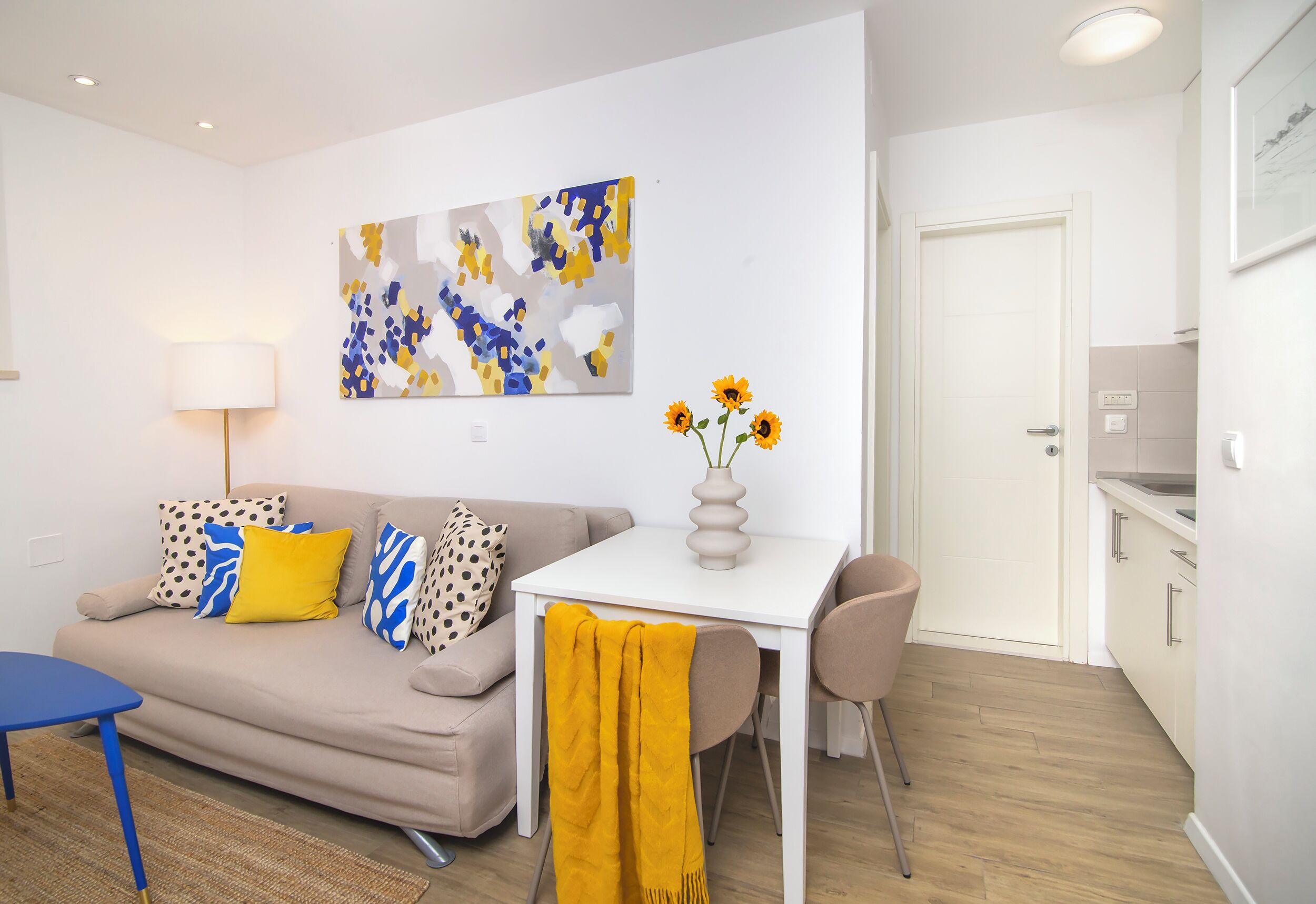 A modern living room with a sofa, a table, and a vase of sunflowers.
