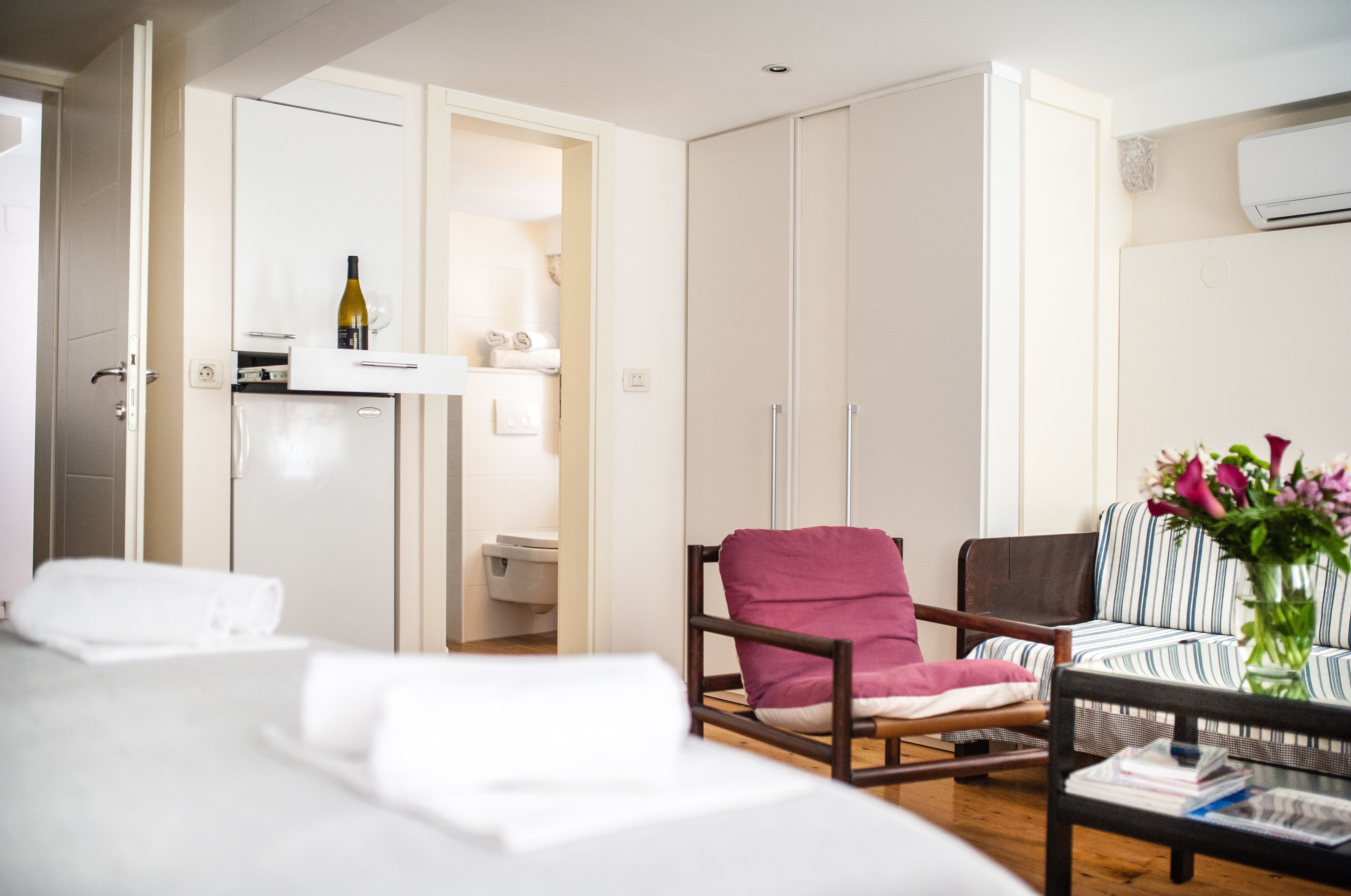 Habitación de hotel con cama, una silla, sofá, una mesita, armario y aire acondicionado instalado en la pared.