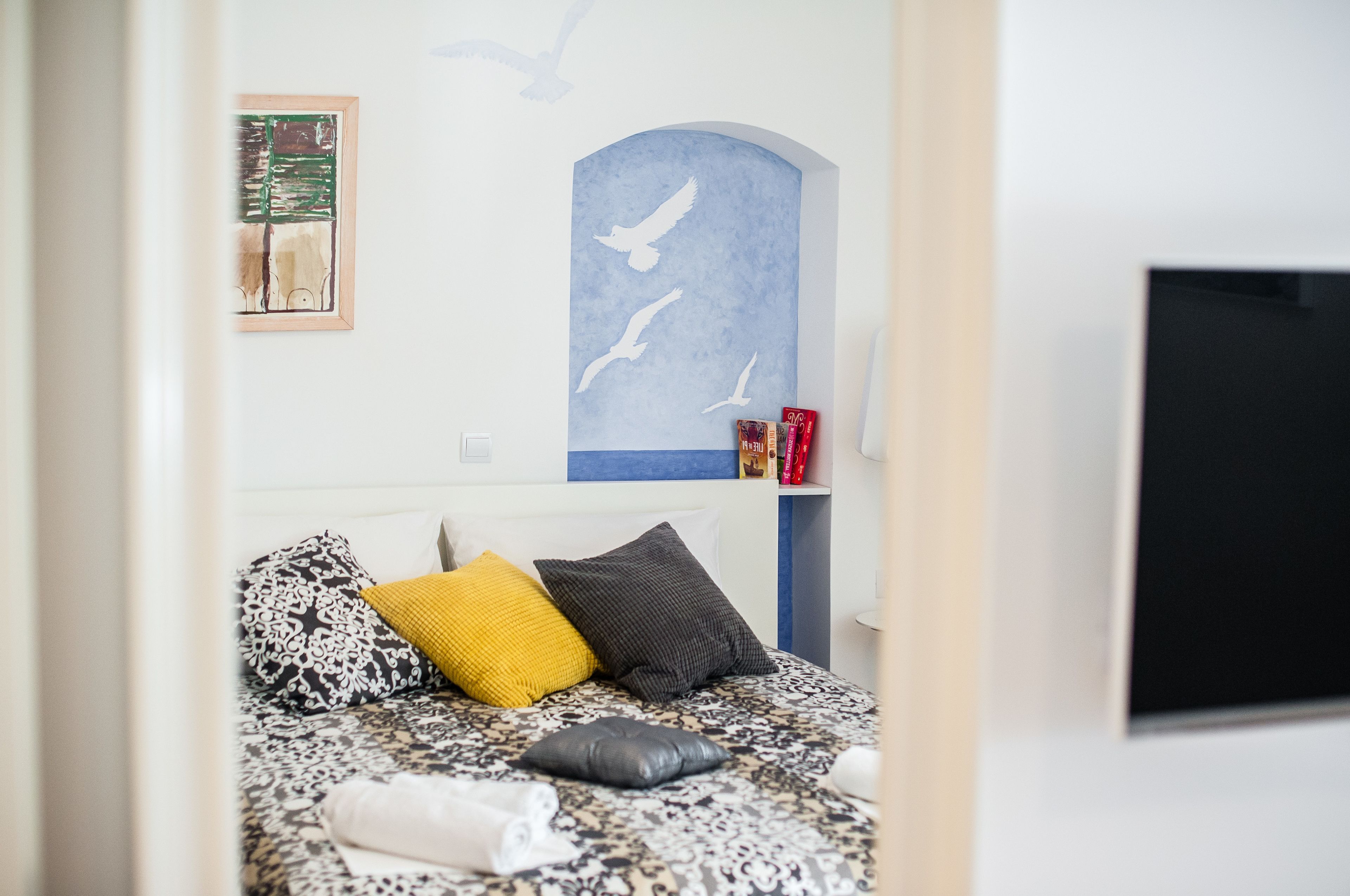 Une chambre à coucher avec un lit, des oreillers, une décoration murale représentant des oiseaux et un téléviseur.