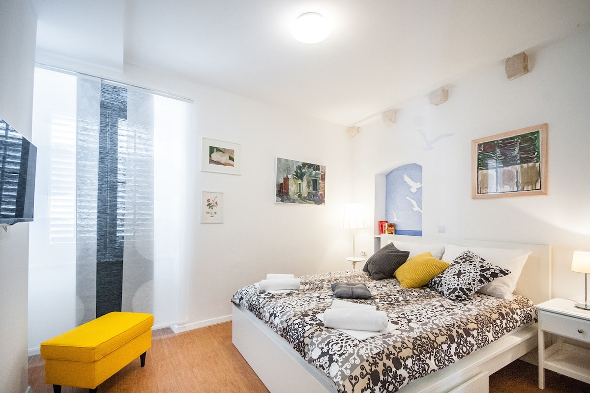 A modern bedroom with a bed, bedside table, and a small yellow bench.