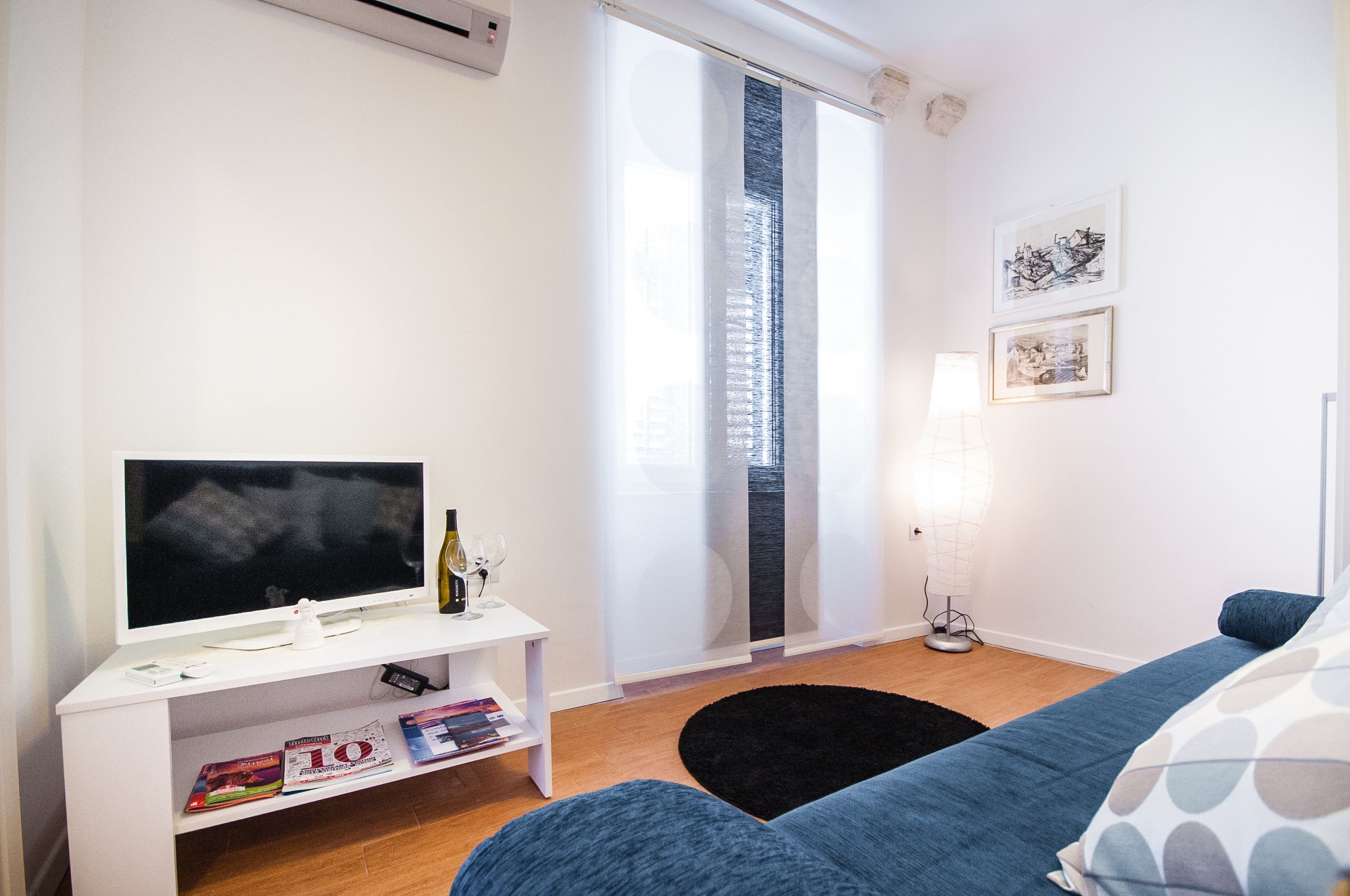 Un salon moderne avec un téléviseur à écran plat, un meuble de rangement blanc, un tapis noir et un canapé bleu.