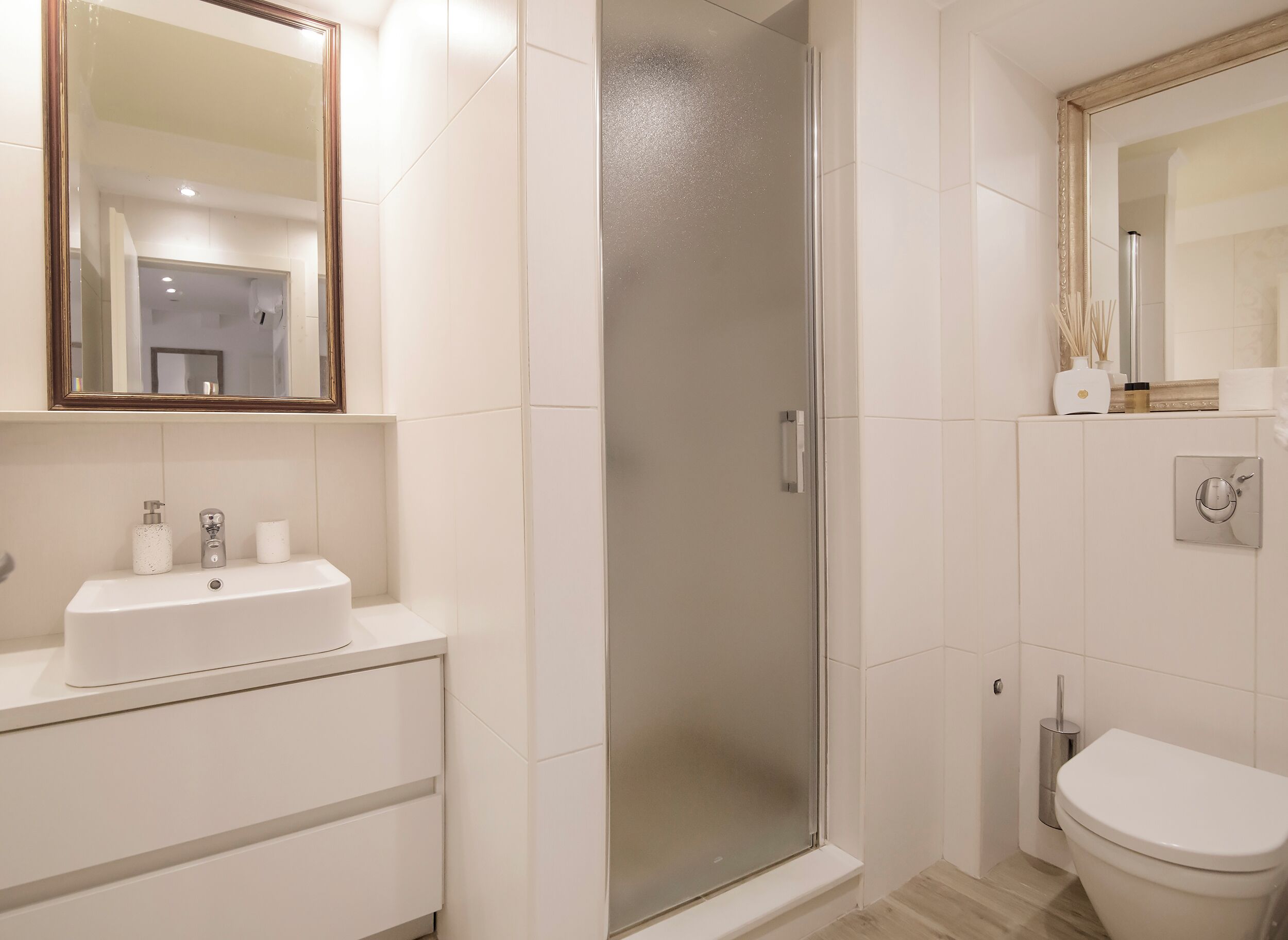 Uma casa de banho moderna com cabine de duche em vidro, uma sanita e lavatório branco com espelho acima.