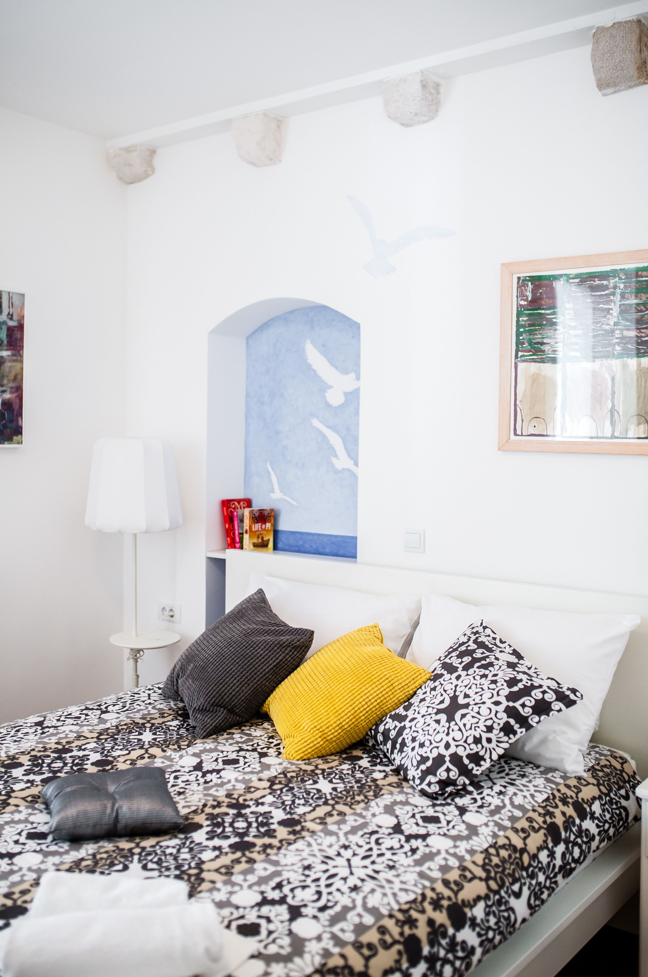 A neatly made bed with patterned bedding, a white lamp, and a framed picture on the wall.