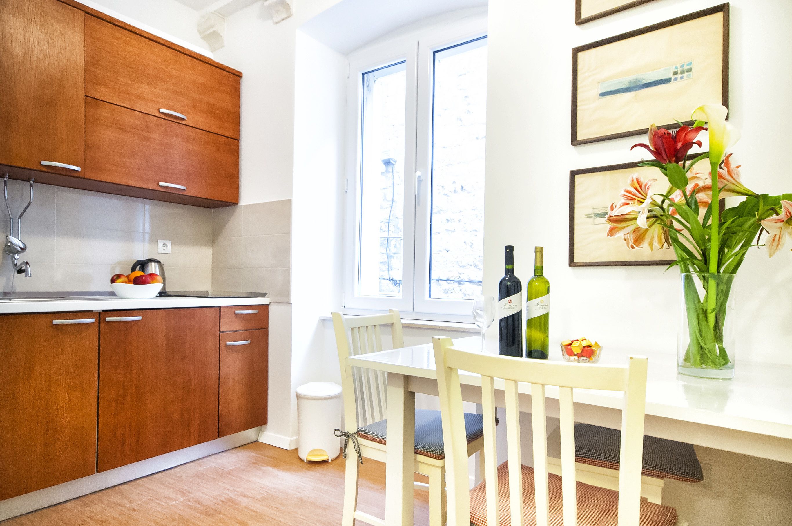 Una cocina con armarios de madera, una mesa de comedor con sillas, un jarrón con flores y una ventana con vistas.