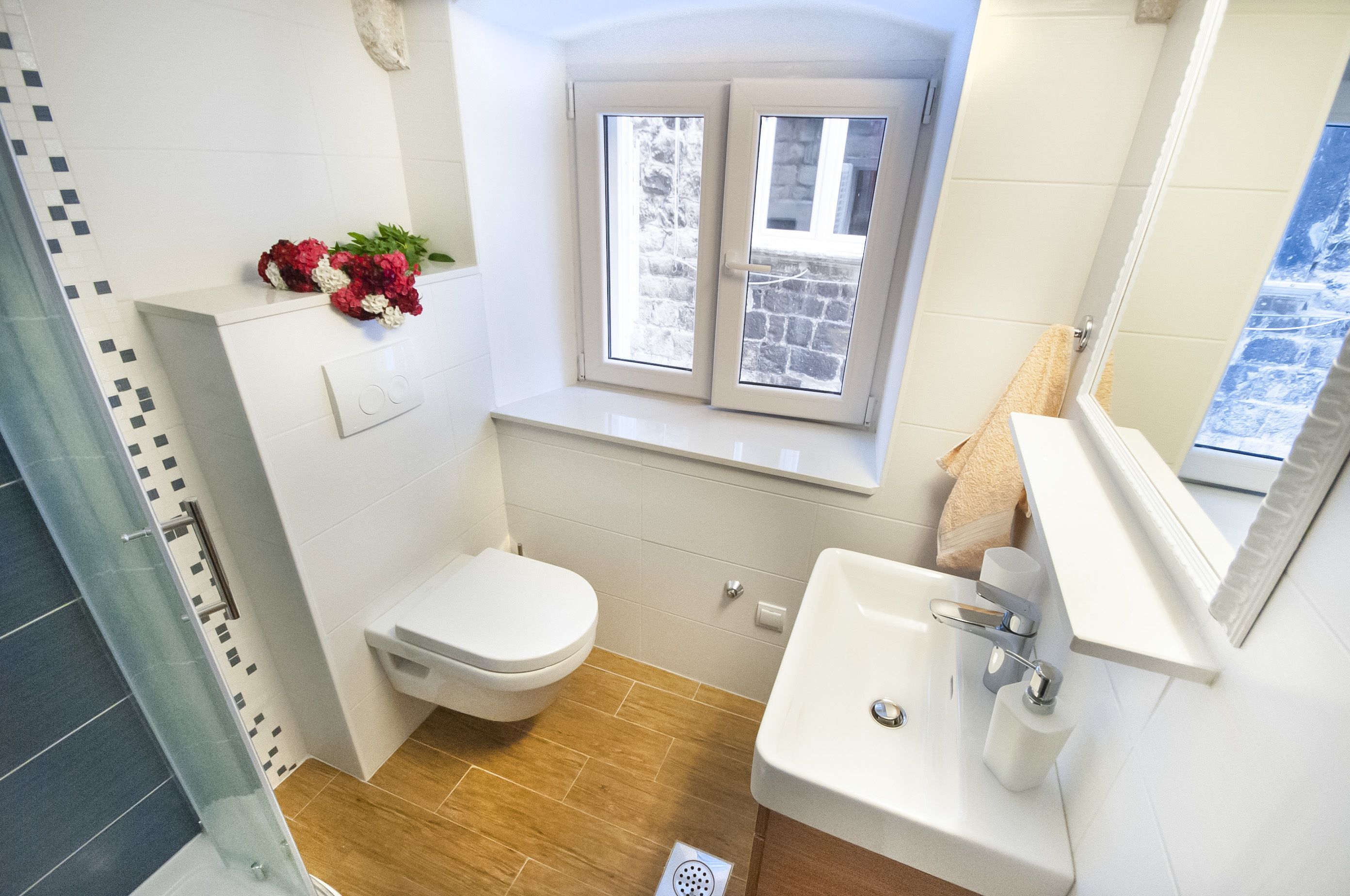 A bathroom with a toilet, sink, and a window with a view of a stone building.