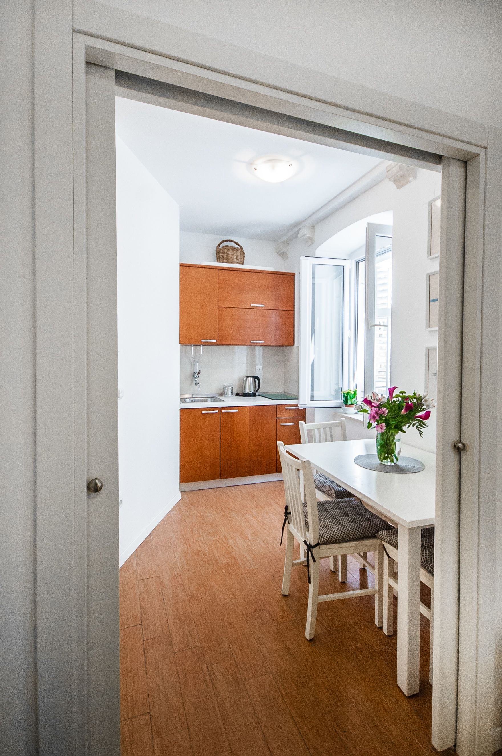 Een moderne keuken met houten kastjes, een eettafel met stoelen en een vaas met bloemen.