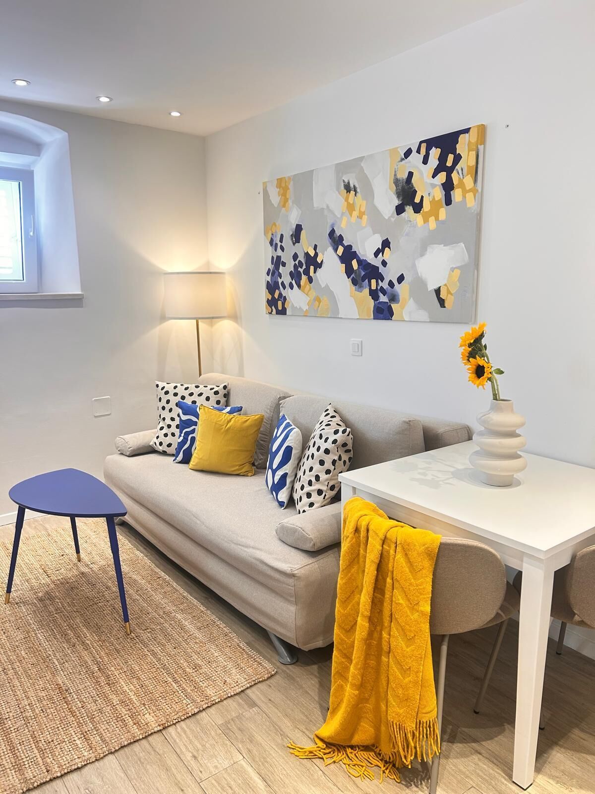 A modern living room with a sofa, a small table, a lamp, and a painting on the wall.