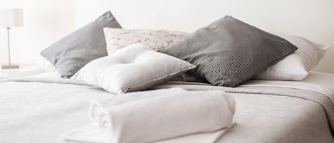 A neatly made bed with a patterned bedspread, two framed artworks depicting coastal scenes, and a bedside lamp.